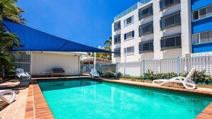 A swimming pool with lounge chairs, a covered seating area, and a building with balconies. - 2 Bedroom Apartment Sea View Second Floor (Sunshine Coast)
