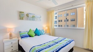 Hotelkamer met een bed, twee nachtkastjes, een plafondventilator, een raam met gordijnen en een schilderij aan de muur.