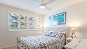A bedroom with a bed, two bedside tables, a ceiling fan, and a window with blinds.