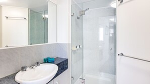Une salle de bain moderne avec un lavabo blanc, une douche en verre et un comptoir en marbre.