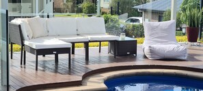 A poolside area with a wicker sofa, a white chair, and a small table. - The Pool House (Lemon Tree Passage)