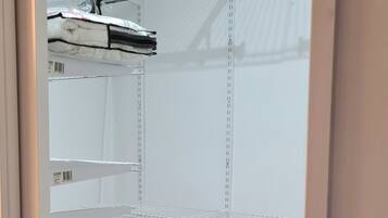 A room with white walls, a metal ceiling, and a tiled floor. There are metal shelves and a metal rod on the ceiling.