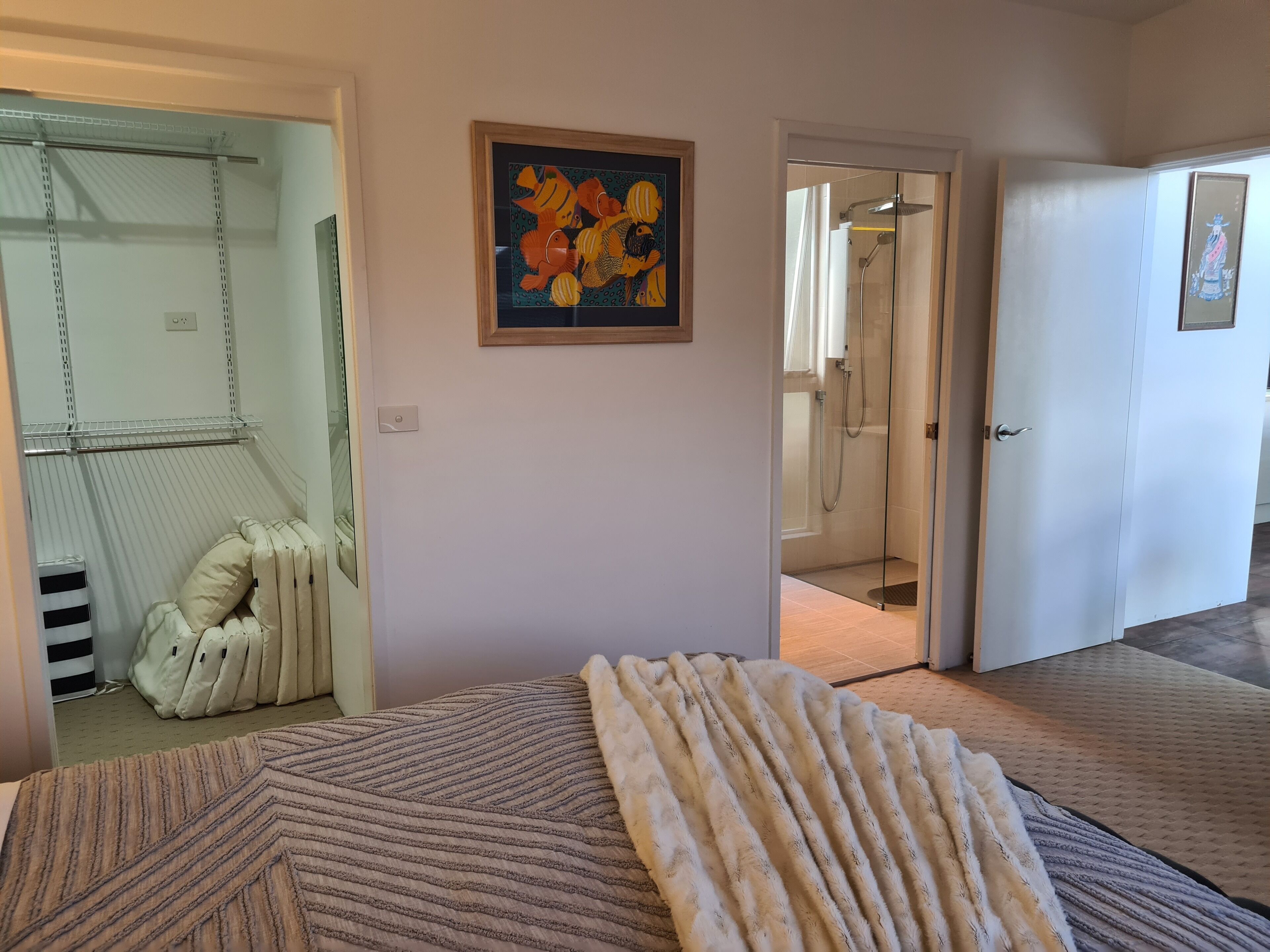 Ein Hotelzimmer mit einem Bett, einem großen Gemälde, einer Duschkabine und einer Tür zu einem weiteren Raum.