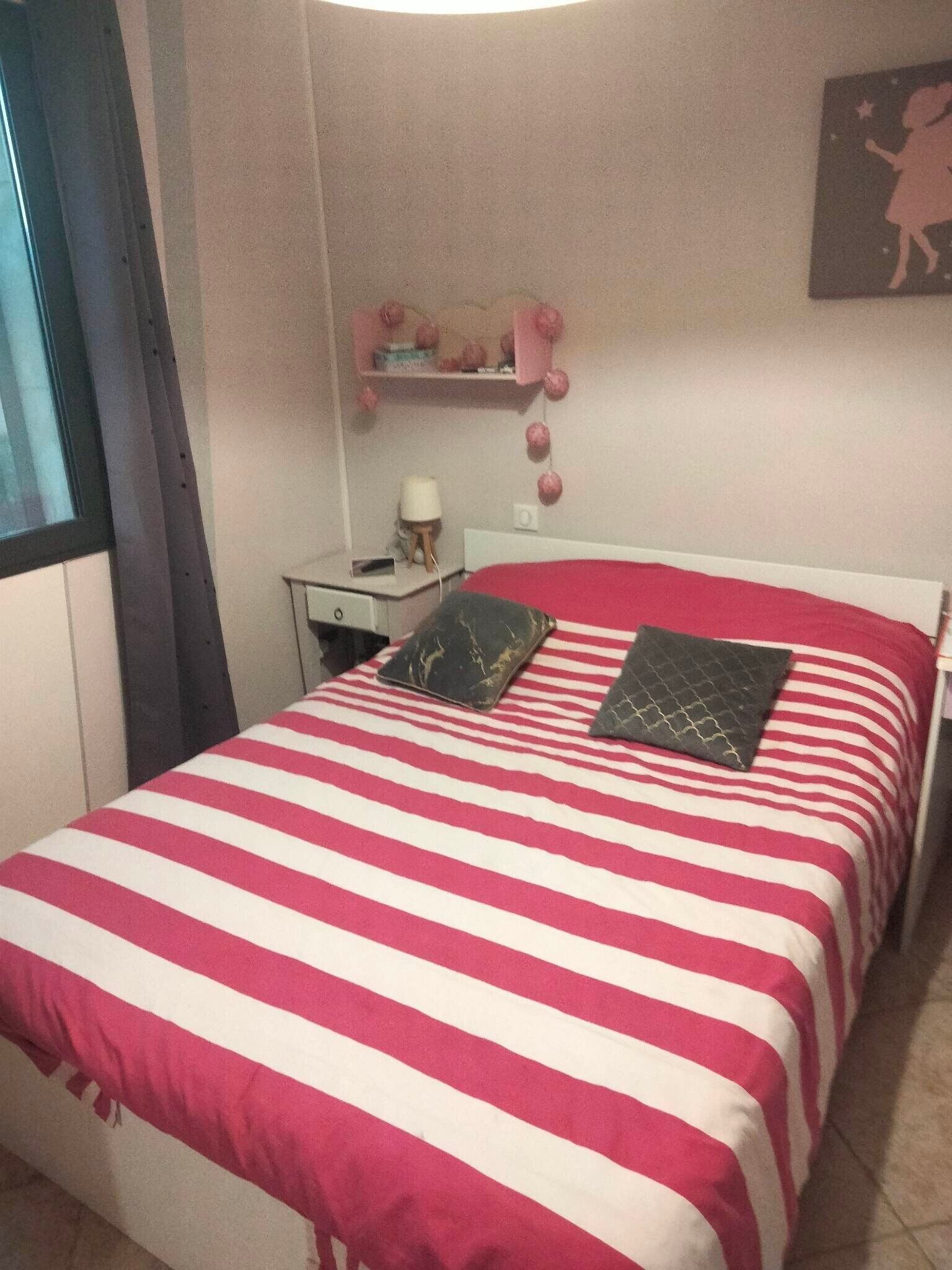 A bed with red and white striped bedding, a nightstand with a lamp, and a wall-mounted shelf with decorative items.