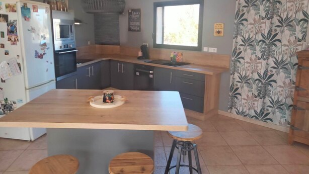 Une cuisine moderne dotée d’un îlot central, de meubles de rangement aux couleurs sombres et d’un luminaire suspendu.