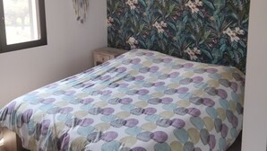 Une chambre à coucher avec un lit, une fenêtre, un mur orné d’un motif floral et un luminaire suspendu.
