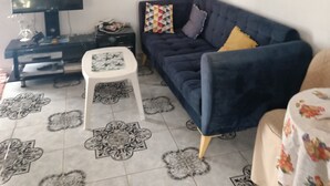 Un soggiorno con un divano blu scuro, un tavolino bianco, una TV a schermo piatto e piastrelle a pavimento decorate.
