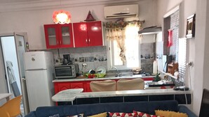 Un ambiente compatto con angolo cottura, un divano con cuscini decorati e un'area pranzo.