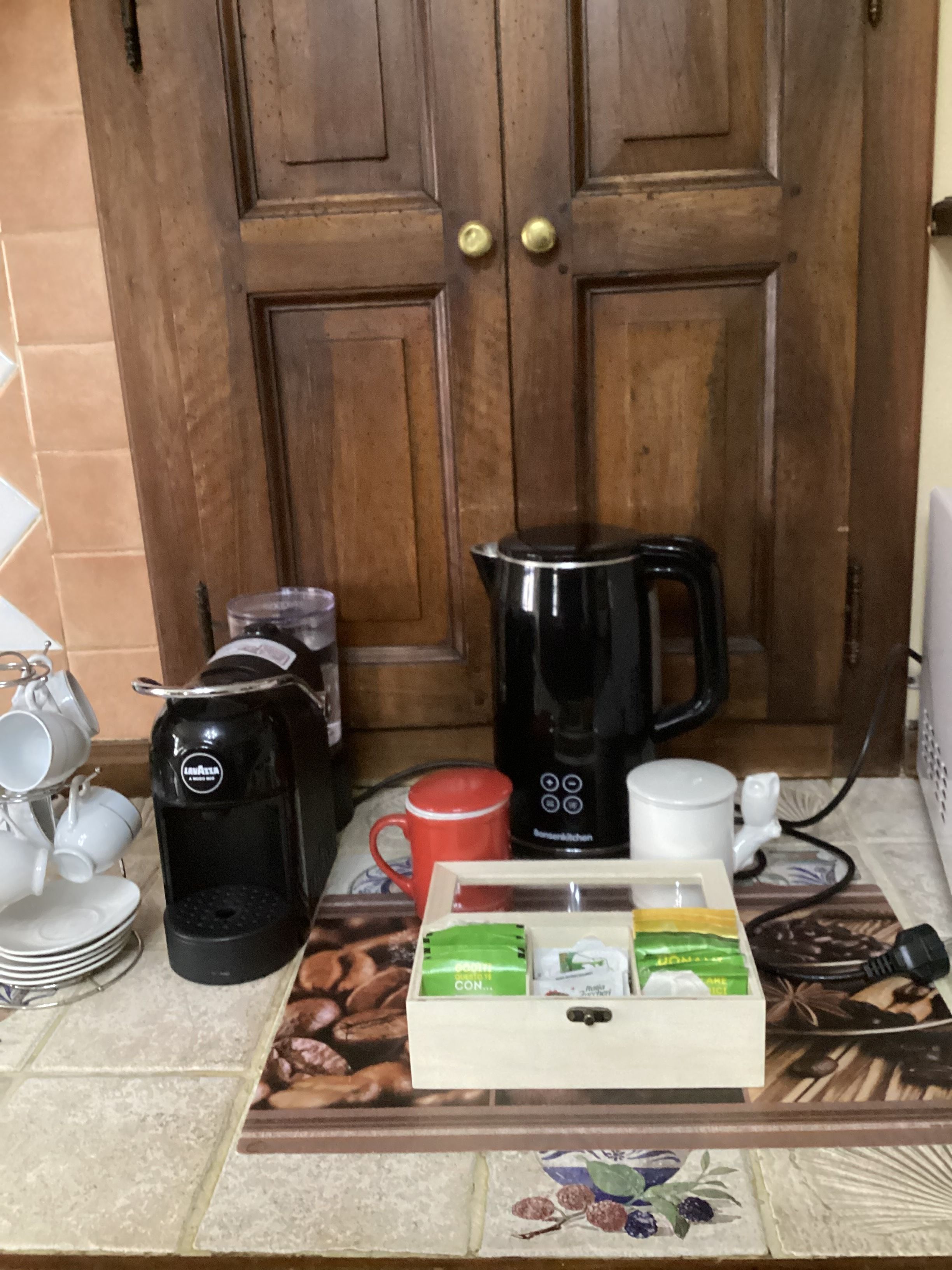 A kitchen counter with a coffee maker, a mug, a box of coffee pods, and a kettle.