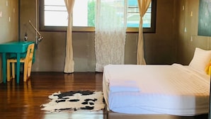 Une chambre avec un plancher en bois, un lit avec une literie blanche, un bureau avec une chaise et un tapis en peau de vache.