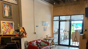 Un vaste espace de vie comprenant un canapé rouge, une table basse et un tableau accroché au mur. Une grande fenêtre laisse entrer la lumière naturelle et offre une vue sur l’extérieur.