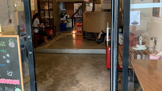 L’intérieur d’un café, avec un comptoir en bois, un menu écrit à la craie et un escalier menant à l’étage.