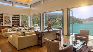 A spacious living room with a large sofa set, a coffee table, and a view of a lake and mountains. - Villa Fah Sai (Kamala)