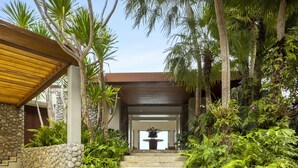A stone staircase leading to a wooden covered entrance, surrounded by lush greenery and palm trees. - Villa Fah Sai (Kamala)