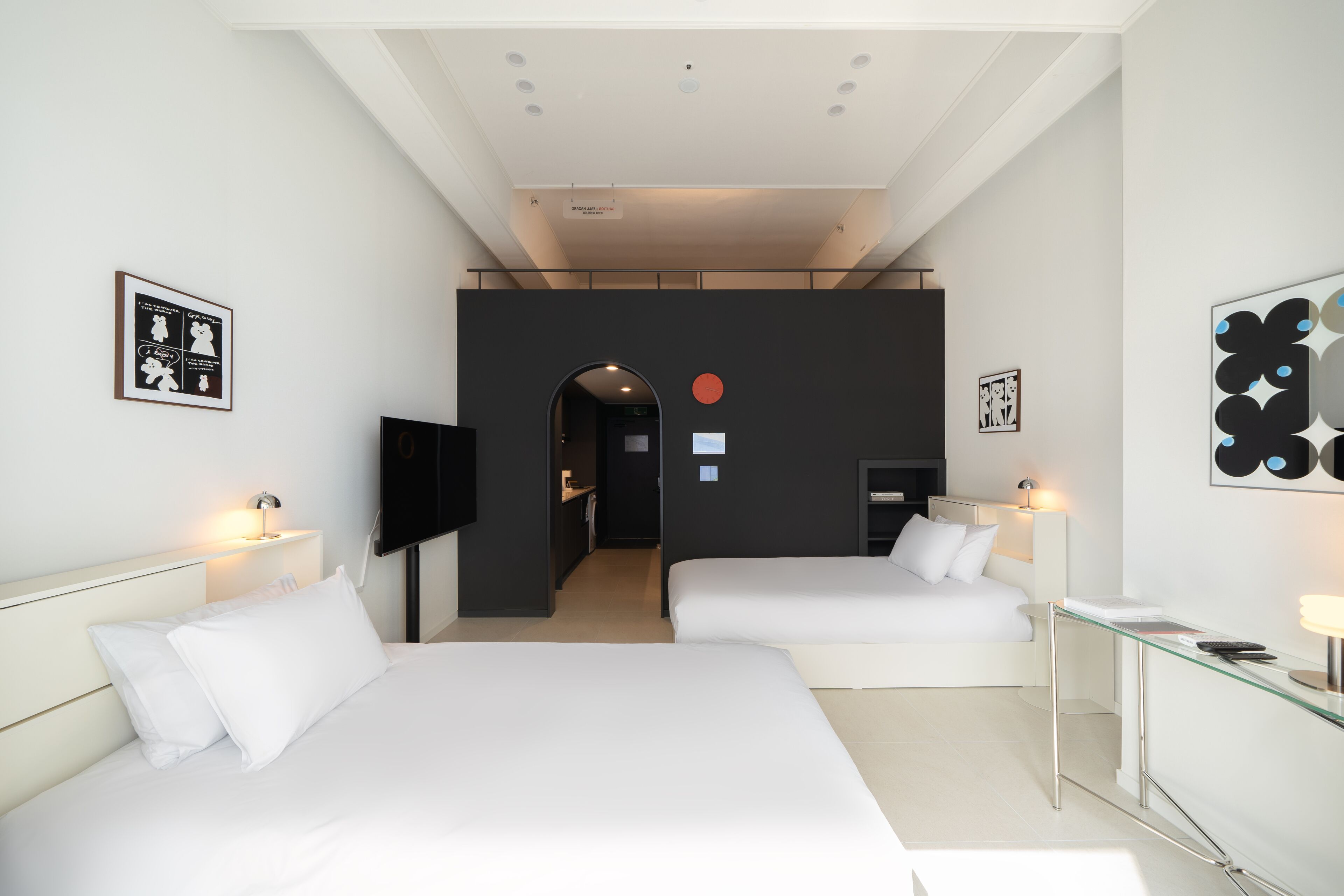 A modern hotel room with two beds, a desk, a TV, and artwork on the walls.