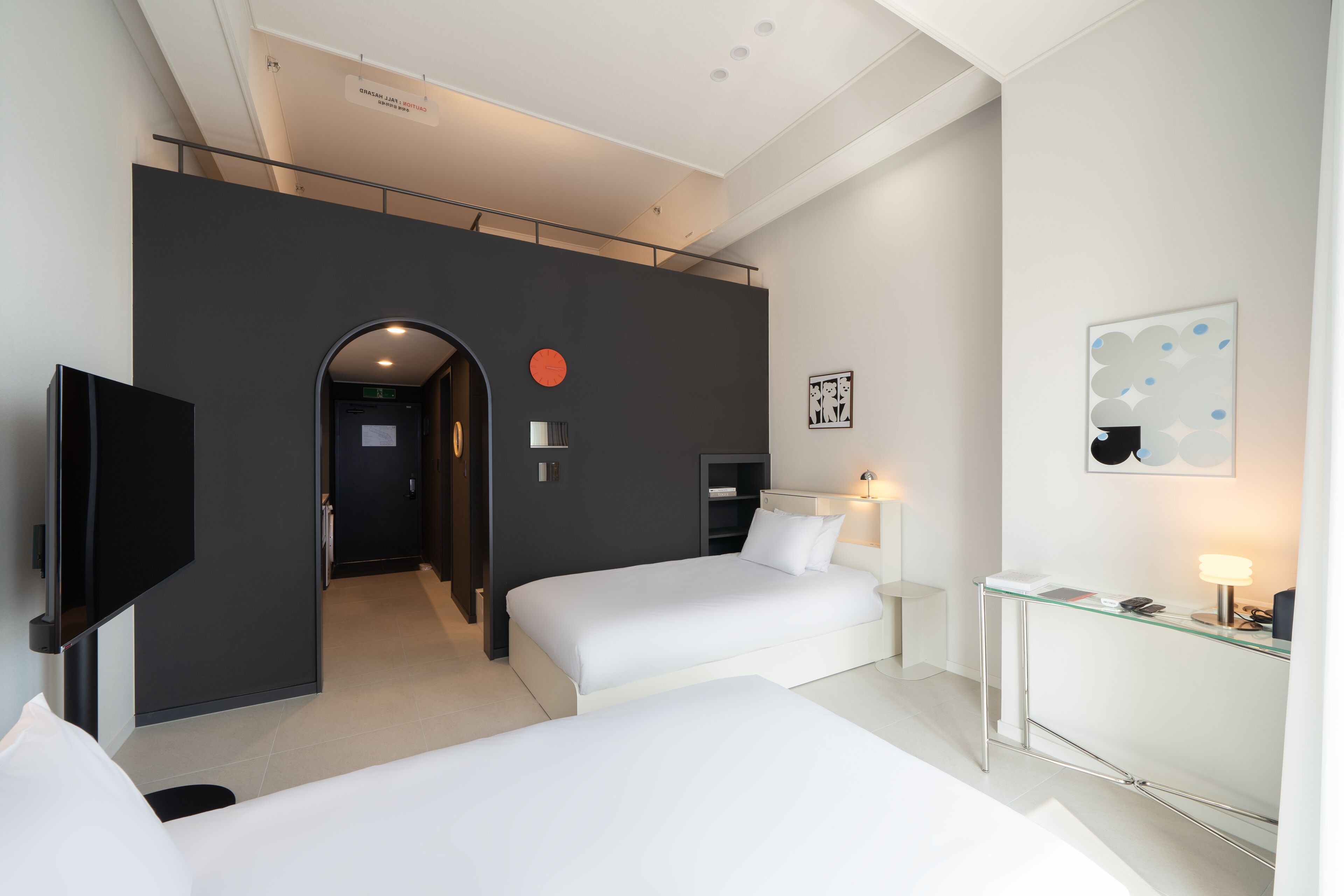 A hotel room with two beds, a desk, a TV, and a bathroom visible through an archway.
