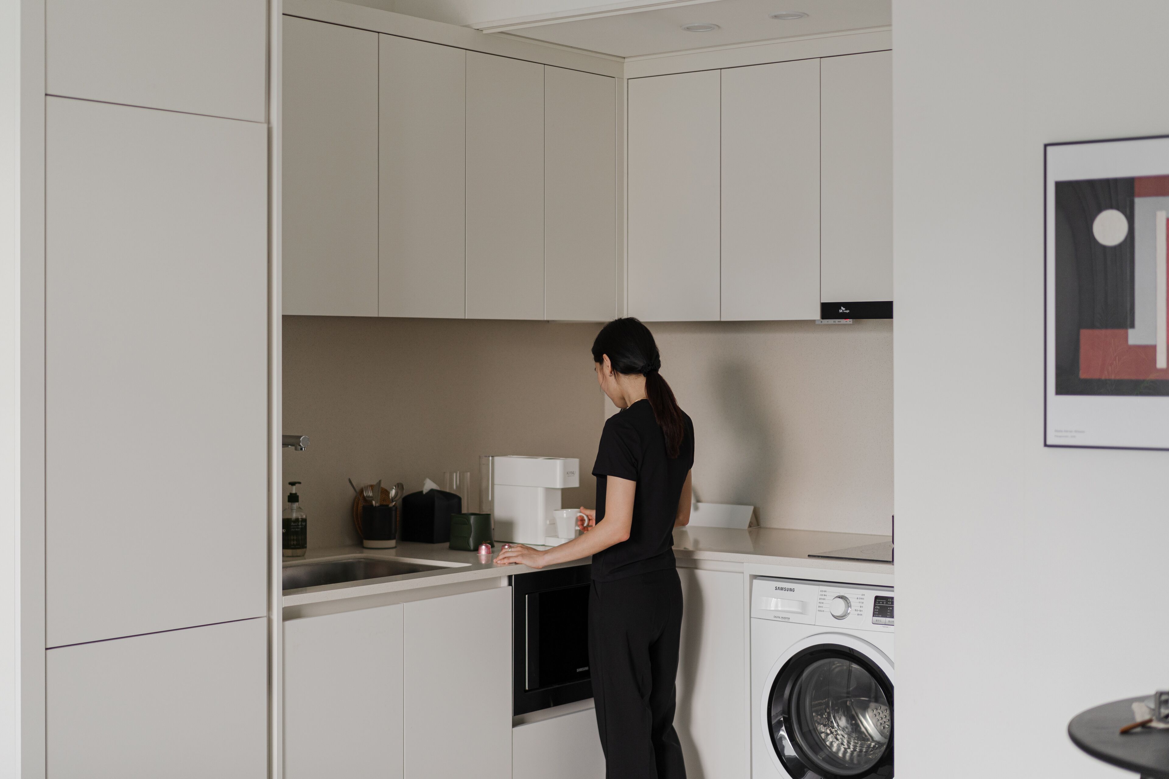 Une cuisine moderne avec des meubles blancs, un lave-linge et une machine à café.