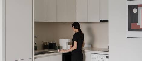 Une cuisine moderne avec des meubles blancs, un lave-linge et une machine à café.