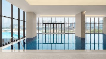 Una amplia piscina interior con vistas despejadas a un paisaje urbano a través de grandes ventanales.