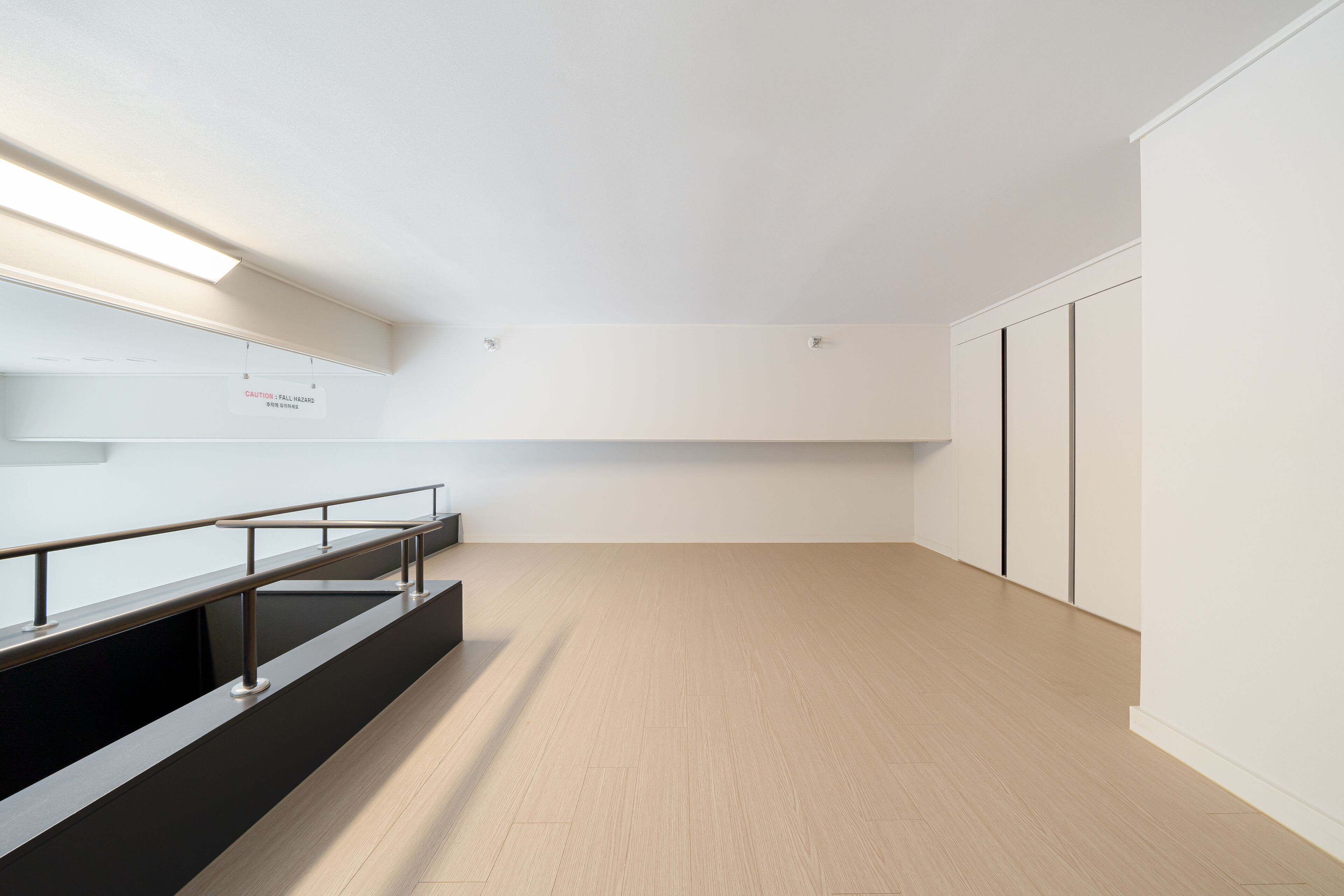 A modern interior with a wooden floor, a black bench, and a white wall with a caution sign.