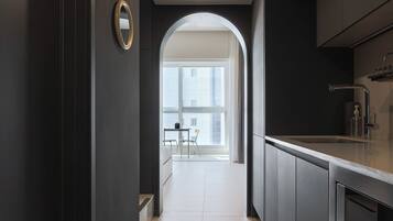 A modern kitchen with dark cabinetry, a stainless steel sink, and a view through an archway to a balcony with a table and chairs.