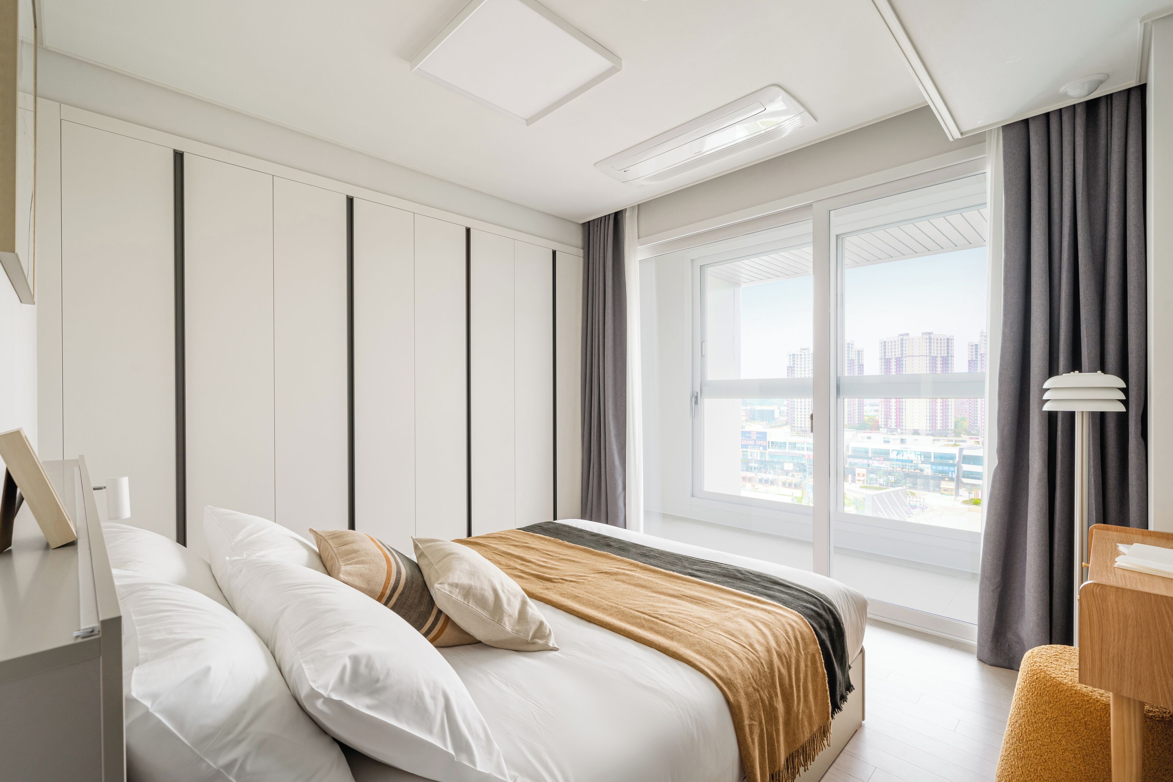 A modern hotel room with a large bed, a desk, and a view of the city through a large window.