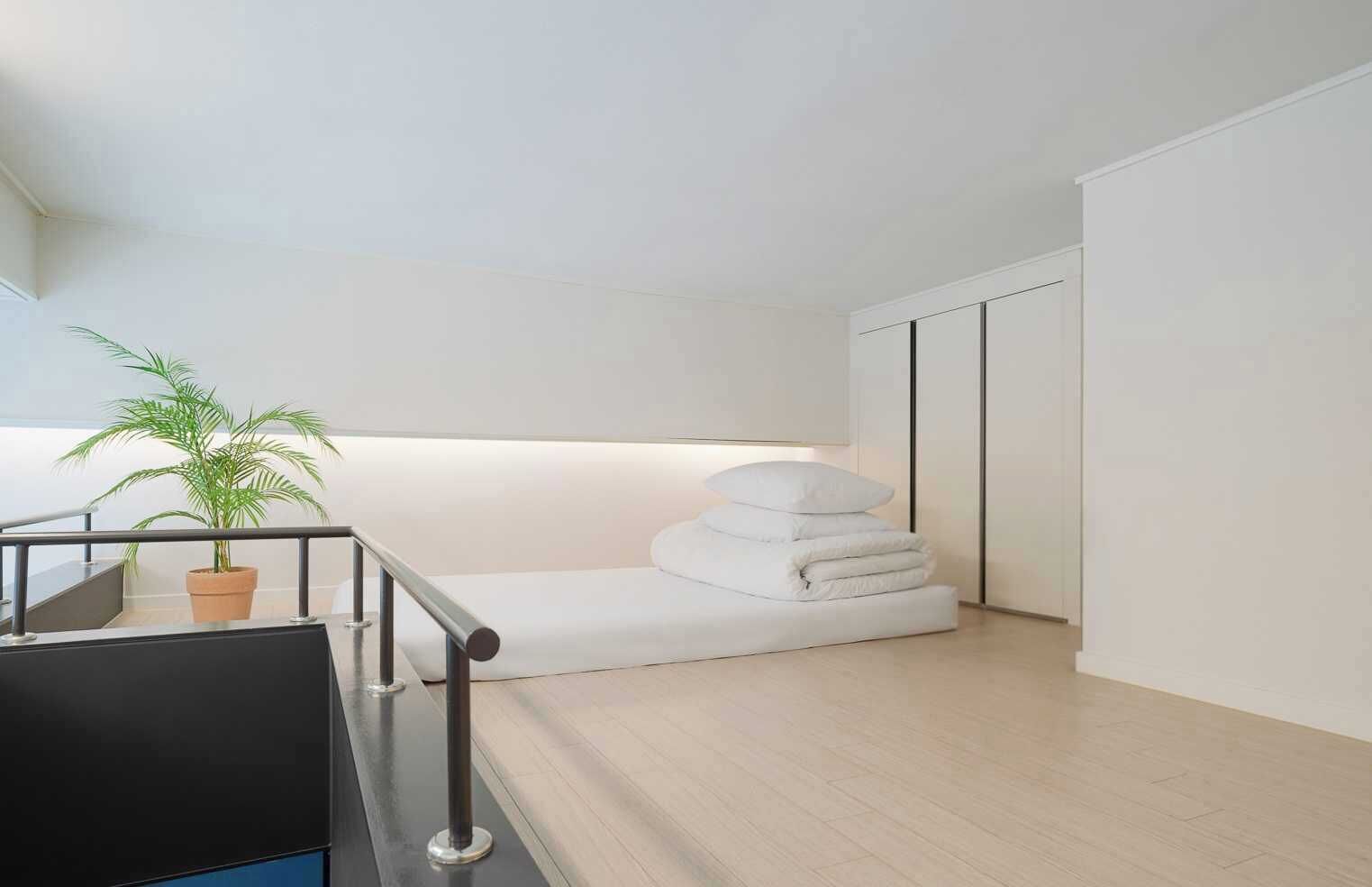 A modern, minimalist room with a staircase, a potted plant, and neatly stacked white pillows.