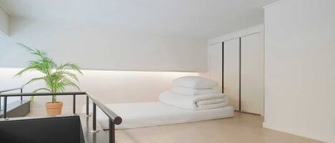 A modern, minimalist room with a staircase, a potted plant, and neatly stacked white pillows.