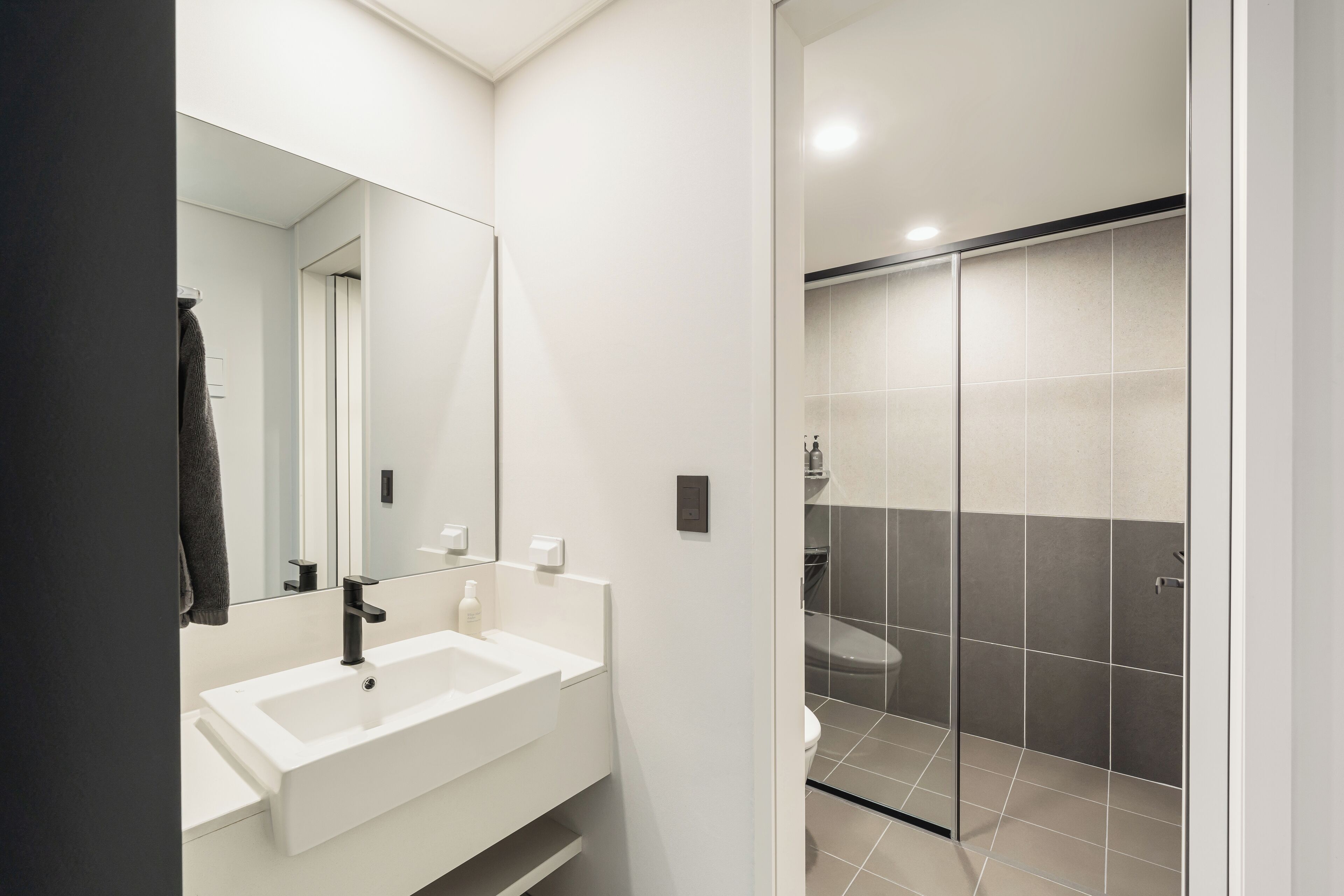A modern bathroom with a white sink, mirror, and shower area.