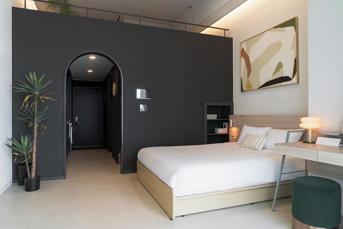 Habitació d'hotel moderna amb un llit, escriptori i prestatgeria.