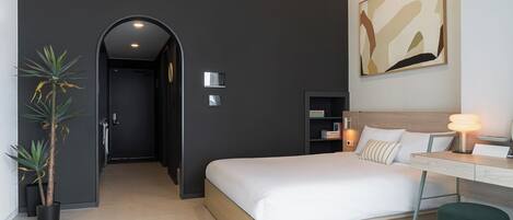 A modern hotel room with a bed, desk, and bookshelf.