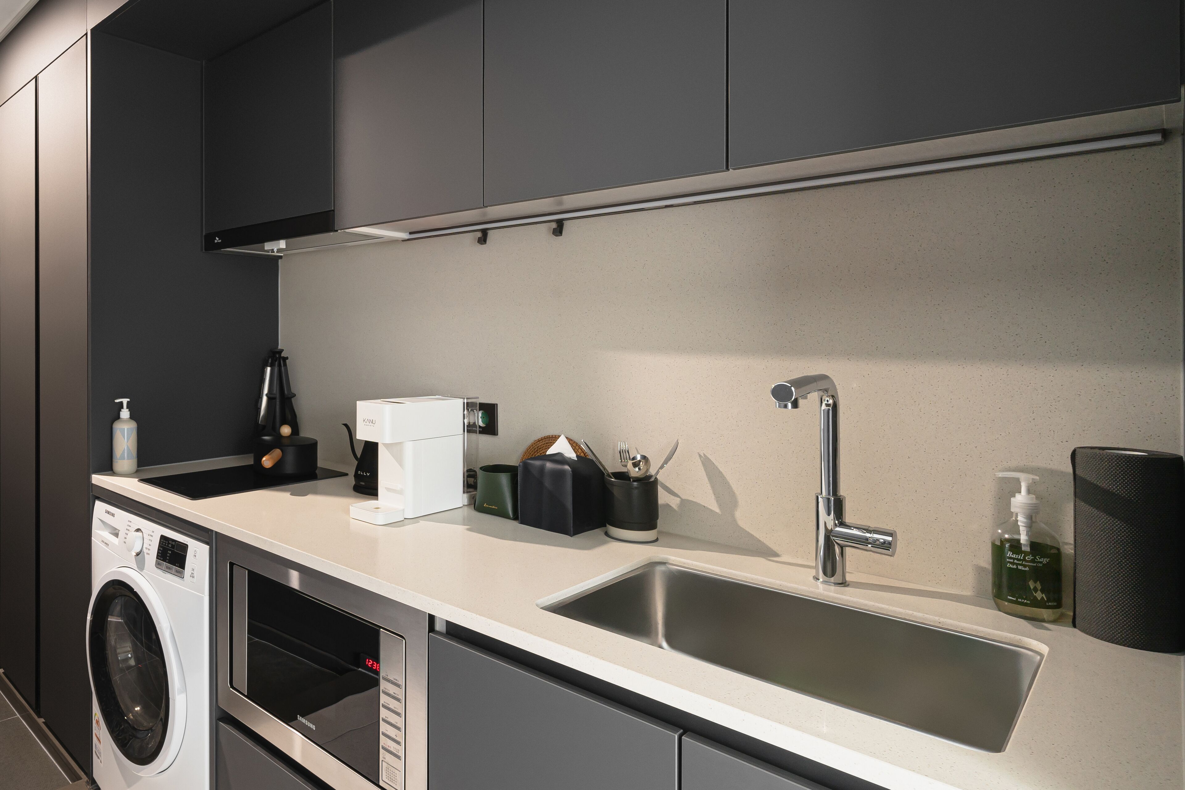 A modern kitchen with a built-in washer and dryer, a stainless steel sink, and a coffee maker.