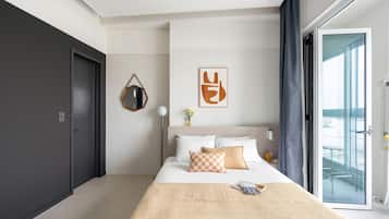 Ein modernes Hotelzimmer mit einem großen Bett, Blick durch eine Glastür und minimalistischer Einrichtung.