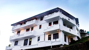 A multi-story white building with balconies, a flat roof, and a stone retaining wall. - Hotel Divyansh By VRB Hotels (Dharamshala)