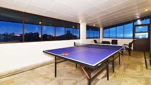 A spacious room with a ping pong table, large windows, and a view of the cityscape at dusk. - Hotel Divyansh By VRB Hotels (Dharamshala)