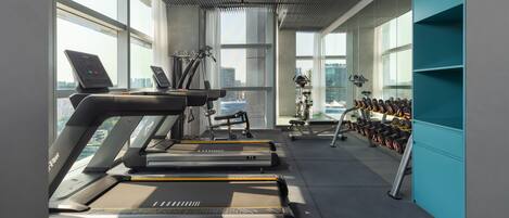 Une salle de sport équipée de tapis de course, de vélos d’exercice et d’une série de haltères.