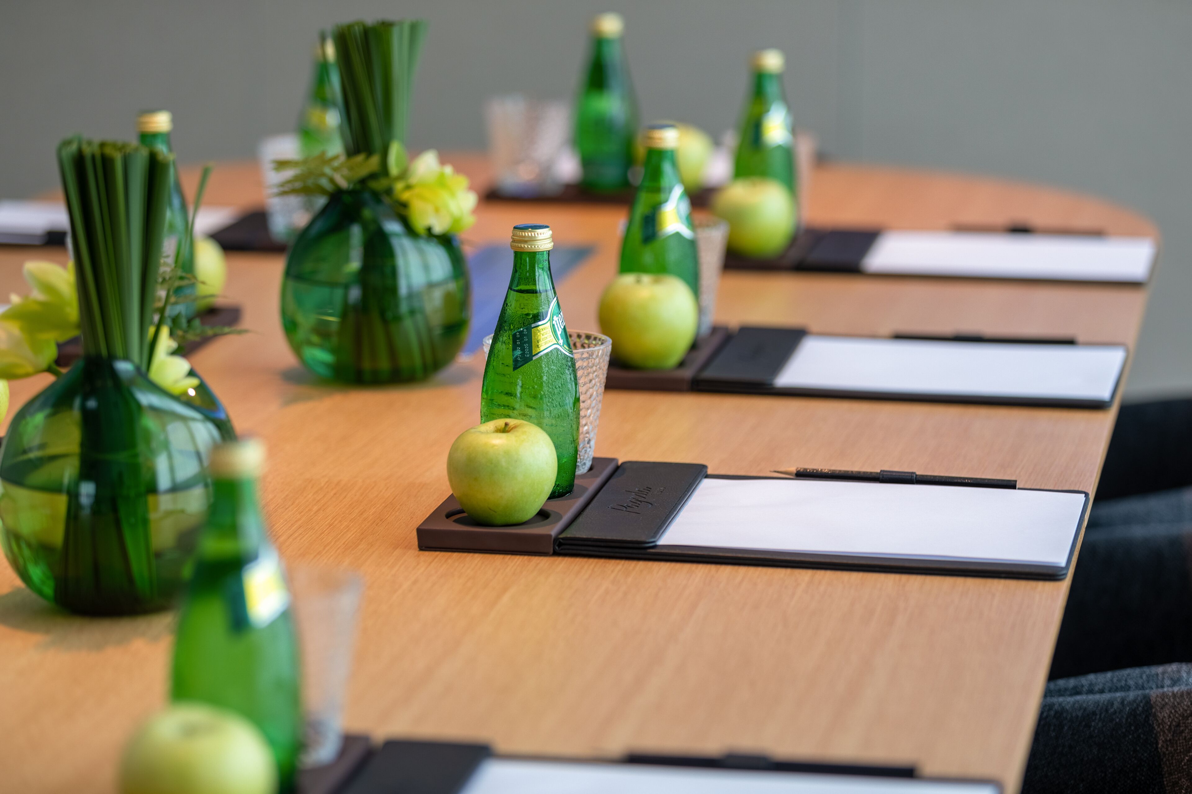 A conference table with green glass bottles, apples, and nameplates.