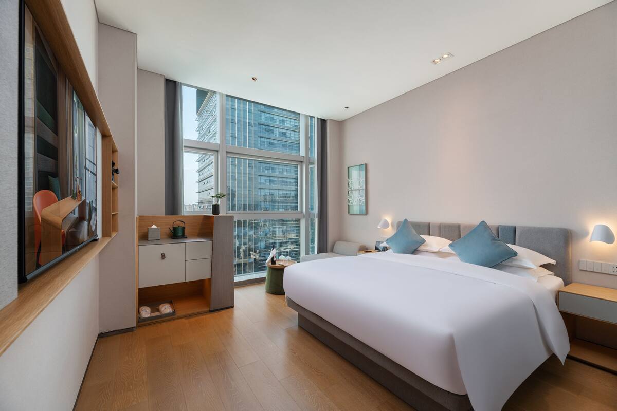 Une chambre d’hôtel moderne, dotée d’un grand lit, d’un bureau et offrant une vue sur la ville grâce à de grandes fen êtres.
