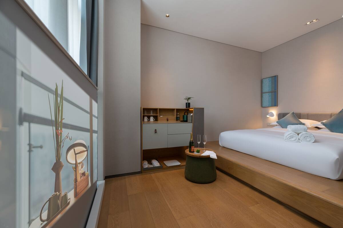 Une chambre d’hôtel moderne dotée d  ’un grand lit, d’un petit coin salon, d’une coiffeuse avec un miroir et offrant une vue sur la ville.