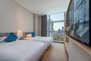 A hotel room with two beds, a large window, and a city view.