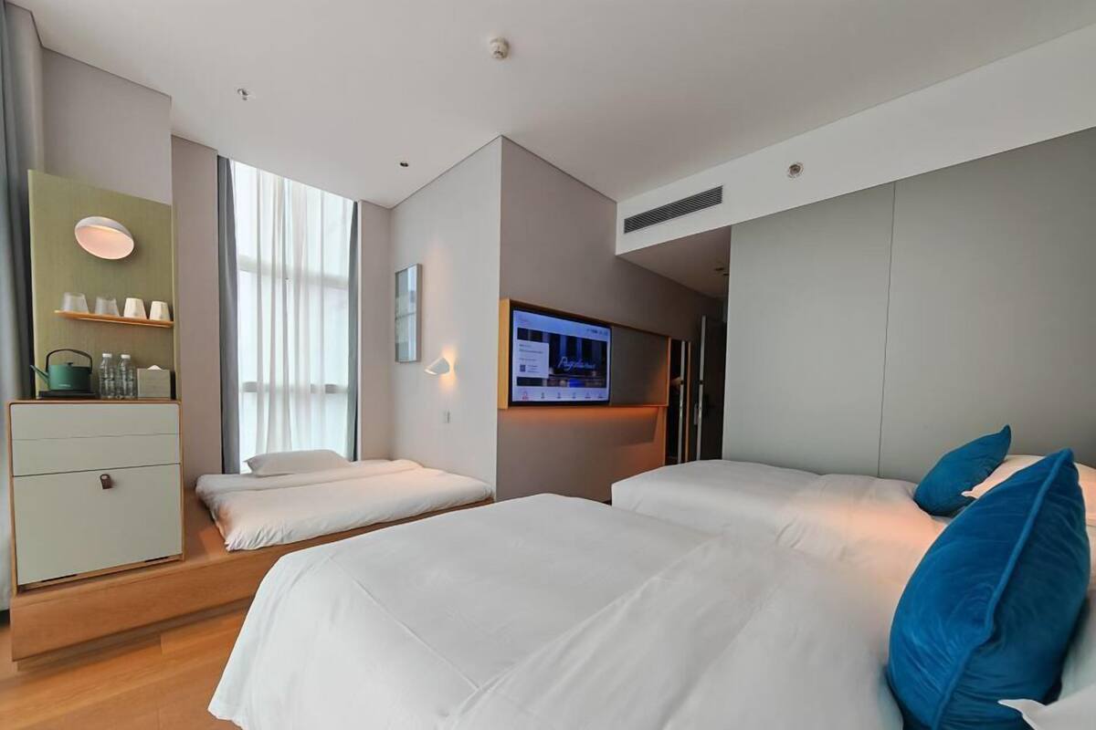 Une chambre d’hôtel moderne équipée de deux lits, d’une télévision, d’un bureau et d’une fenêtre avec des rideaux.