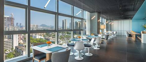 A modern dining area with large windows, multiple tables, and chairs.