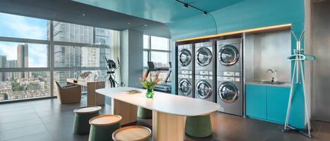A modern, well-lit laundry room with large windows, a central table, and multiple washing machines.