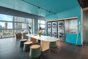 A modern, well-lit laundry room with large windows, a central table, and multiple washing machines.