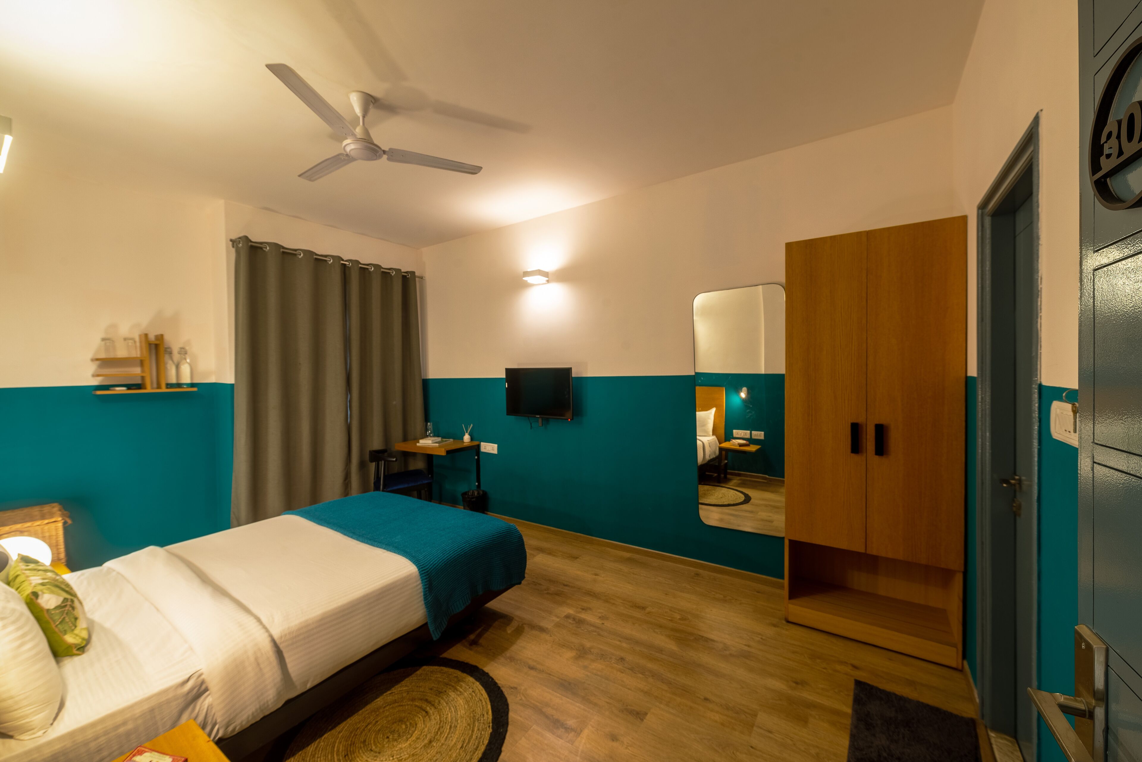 Una habitación de hotel con cama, ventilador de techo, televisión, armario y espejo.
