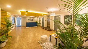 A modern reception area with a wooden floor, a reception desk, and potted plants. - Olive Hotel Magrath by Embassy Group (Bengaluru)