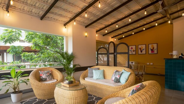 A cozy lounge area with wicker furniture, a potted plant, and artwork on the wall. - Olive Hotel Magrath by Embassy Group (Bengaluru)
