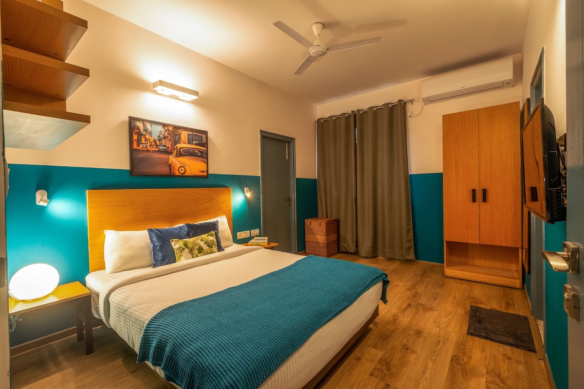 Habitación de hotel con cama, mesita de noche, ventilador de techo, un cuadro, armario y baño con cortina de ducha.