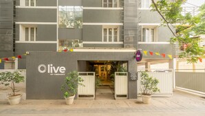 A hotel entrance with a 'Live by Embassy' sign, potted plants, and a gated entrance. - Olive Hotel Magrath by Embassy Group (Bengaluru)