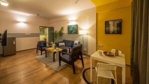 A modern living room with a sofa, chairs, a coffee table, and a dining table. There is a ceiling fan, a lamp, and a painting on the wall. - Olive Hotel Magrath by Embassy Group (Bengaluru)
